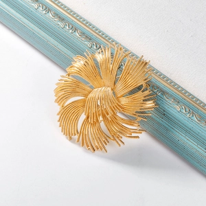 Close-up of golden floral tassel brooch with intricate metal wire textures on white surface