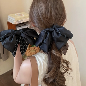 Detail of a large black satin bow hair clip with leopard print and polka dot ribbon patterns