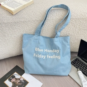 Dettaglio della borsa tote in denim azzurro con scritta ricamata Blue Monday bianca