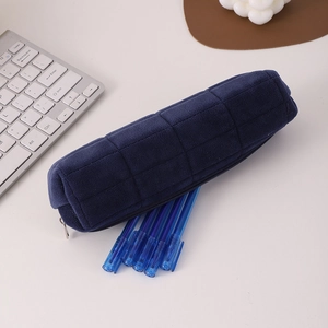 Close-up of dark blue quilted pencil case with blue pens on a clean white desk