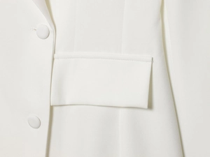 Détail d'un blazer blanc croisé montrant la texture du tissu et un bouton recouvert de tissu