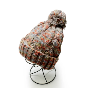Detail of multi-color cable knit winter hat with grey faux fur pom pom on a metal stand