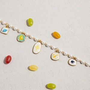 Macro detail of 18K gold stainless steel chain with celestial enamel charms and pearls
