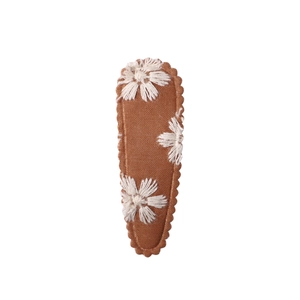 Detailed view of a brown fabric hair clip featuring white embroidered floral patterns