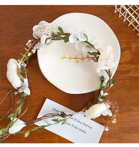 Close-up of white floral headband with green leaves and woven vine base on wood