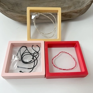 Square floating film jewelry display boxes in yellow, pink, and red with necklaces