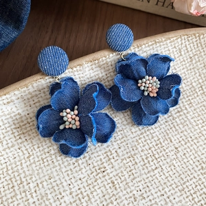 Detailed macro of denim flower earrings with colorful beads on a ceramic tray