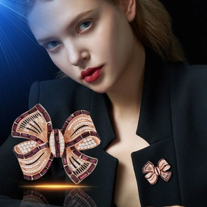 Close-up of rose gold bow brooch featuring deep red gemstones and clear diamonds on a suit