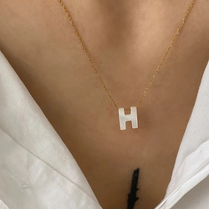 Gros plan détaillé du collier à pendentif H doré avec nacre blanche sur une chemise