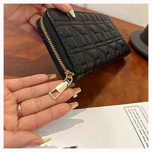 Close-up of black quilted leather wallet with gold zipper detail on a wooden table
