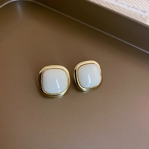 Detailed close-up of square gold-rimmed cream pearl earrings on a bronze vintage tray