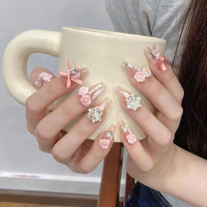 Handmade pink press-on nails with 3D roses, bows, and pearls on a model's hand