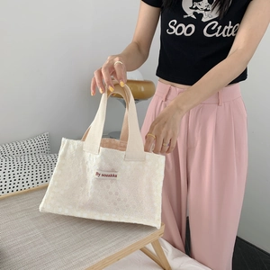 Close-up of white canvas lunch bag with intricate floral lace and red brand label