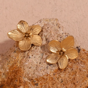 Detail of 18K gold-plated flower stud earrings with textured petals on a stone