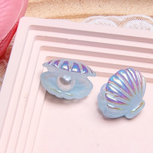 Detailed view of iridescent blue resin shell charms with white pearl on pink display