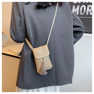 Model wearing a beige straw woven crossbody bag with stylish tassel fringe detail