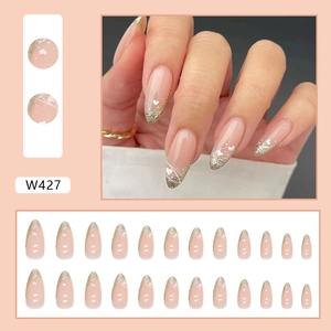 French almond press-on nails with champagne gold glitter edges and heart patterns