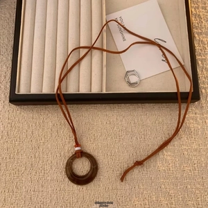 Detail einer Bohème-Langen-Kette mit braunem Harzring-Anhänger auf gewebter Textur
