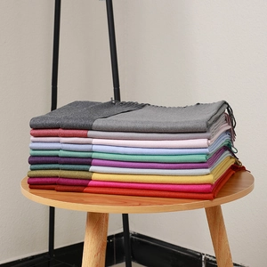 Stack of colorful scarves with tassel edges in various shades on a wooden table