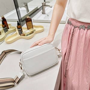 Detail of white litchi pattern bag with striped wide strap on marble surface