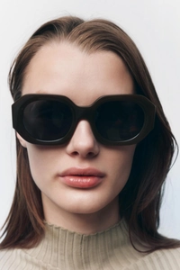 Close-up of a model wearing dark hexagonal sunglasses with thick retro acetate frames