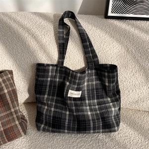 Detail of classic black and white plaid tote bag with logo patch on soft textured surface