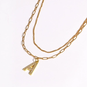 Detail view of a layered gold necklace featuring a zircon-encrusted 'A' letter pendant
