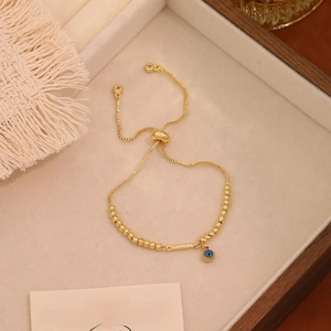 Dettaglio del bracciale regolabile con perline dorate, malocchio e barra di strass