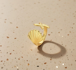 Detail of gold seashell and starfish adjustable titanium ring on sandy background