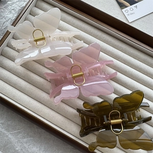 Detailed view of three butterfly hair claws in cream, pink, and dark green colors