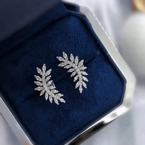 Elegant feather-shaped crystal stud earrings set in a navy blue velvet jewelry box