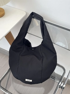 Sac cabas noir plissé en forme de croissant avec étiquette tissée sur chaise acrylique