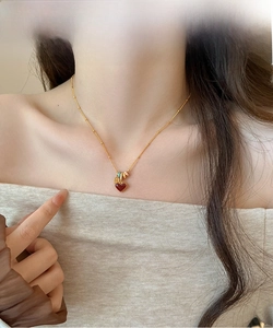 Detail showing an 18k gold plated necklace with a red heart pendant on a female model