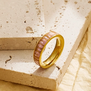 Detail of gold zircon ring with pink baguette stones on a beige stone background