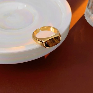 Macro detail of vintage gold oval tiger eye ring resting on an iridescent white ceramic dish