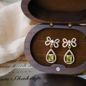 Detail of zircon bow earrings with teardrop gems displayed on a walnut jewelry box
