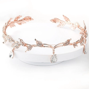 Rose gold leaf bridal crown with sparkling crystals and teardrop pendants on white stand