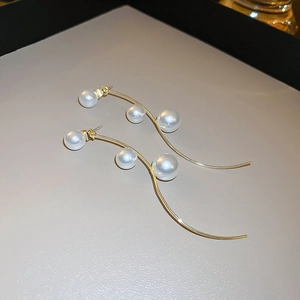 Detail of elegant gold S-shaped wave earrings with three white pearls on a minimalist tray
