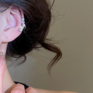 Détail d'un ear cuff élégant avec trois perles blanches et deux strass brillants sur l'oreille