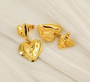 Close-up of gold double-layered heart earrings on a textured white fabric backdrop