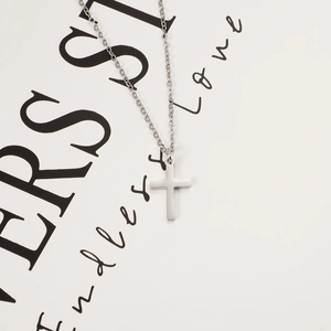 Polished stainless steel cross pendant necklace with classic chain on minimal white card