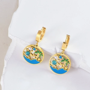 Boucles d'oreilles palmier dorées avec perles turquoise sur un plateau en pierre
