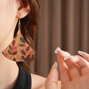 Close-up of bohemian fan-shaped cork earrings with red and black leaf prints and gold hooks
