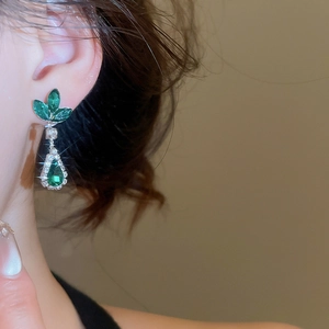 Detailed view of teardrop emerald earrings featuring diamond-encrusted leaf motifs