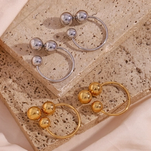 Detail of 18K gold and silver triple ball hoop earrings on a textured stone tray