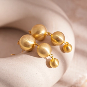 Detailed close-up of golden matte metal bead drop earrings with a minimalist geometric design