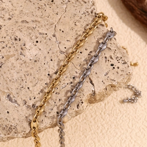 Detail of coffee bean link chain in gold and gunmetal finish on a stone surface