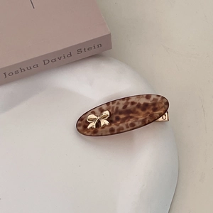 Close-up of leopard print oval hair clip with gold bow accent on a white tray