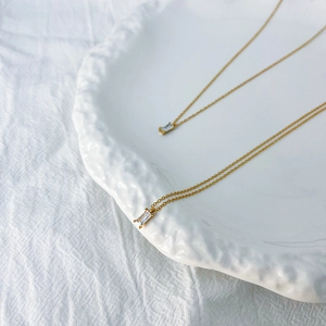 Detail of gold chain necklace with rectangular clear zircon pendant on a white ceramic plate