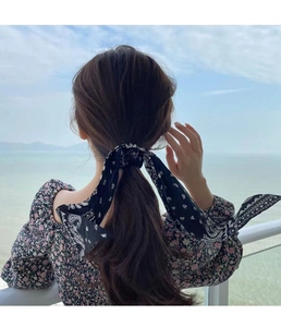 Detail of a black paisley silk hair scarf tied in a bow style for a summer look